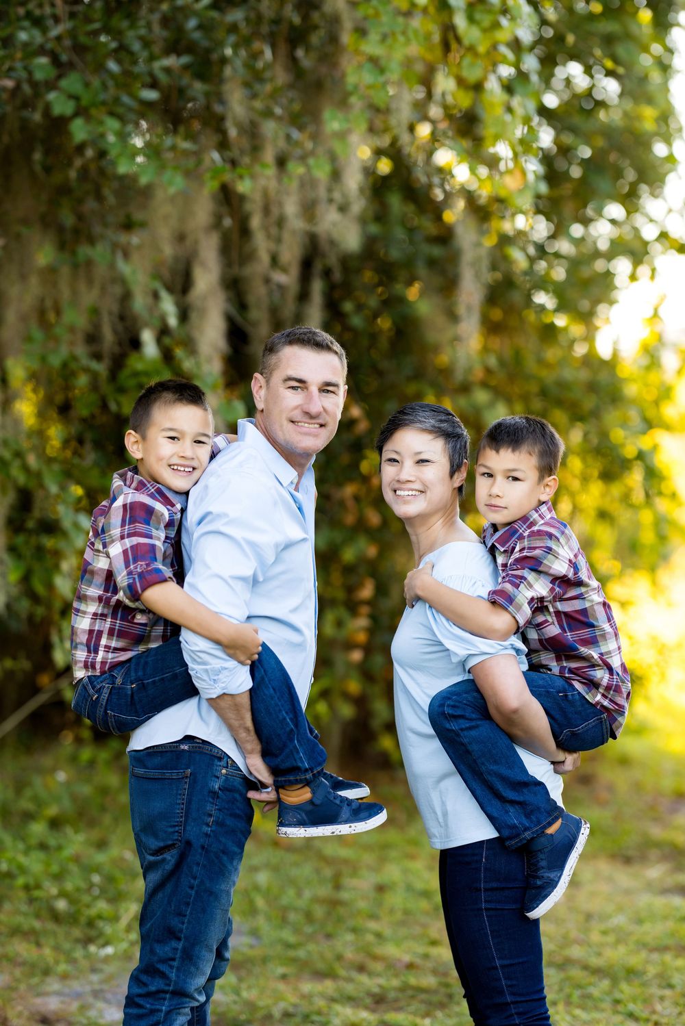 A family poses together outdoors in matching outfits with parents holding children against a natural backdrop.