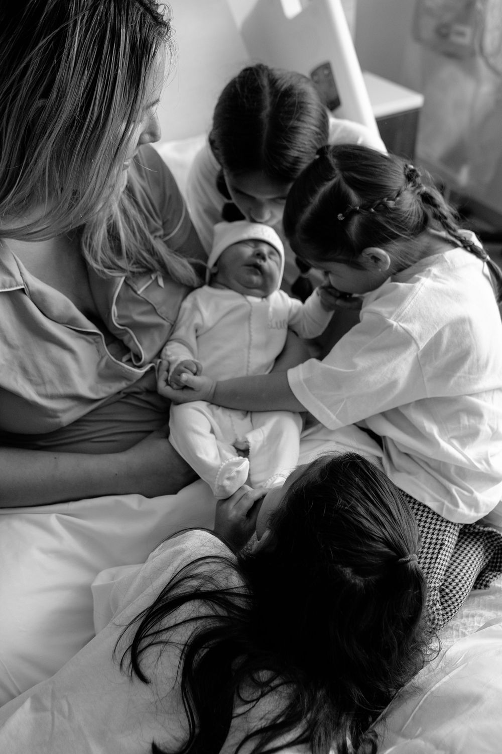 Black and white image of a newborn baby being cradled in a hospital bed surrounded by family members.
