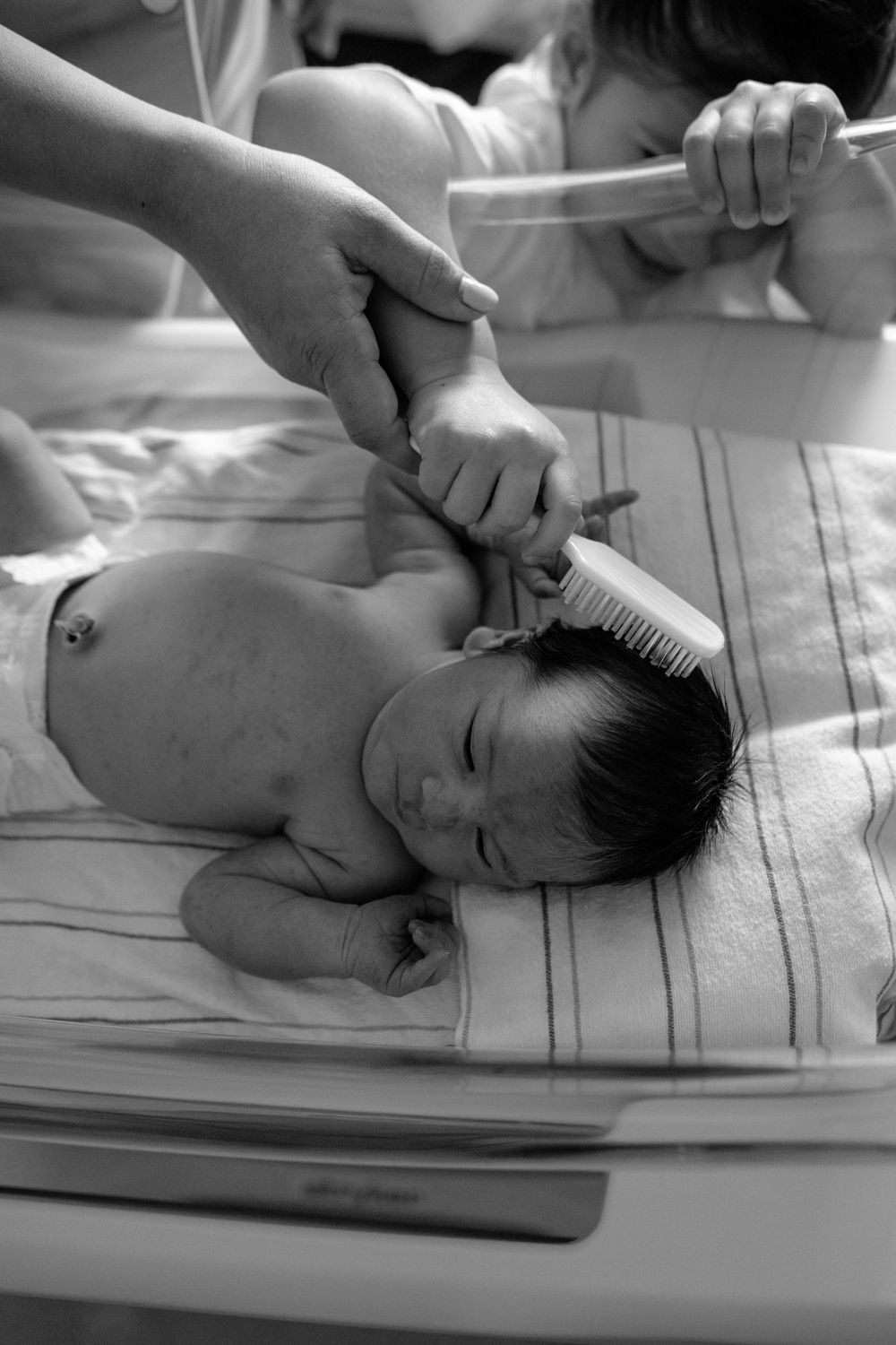 Black and white image of a newborn baby being examined on a hospital bed.