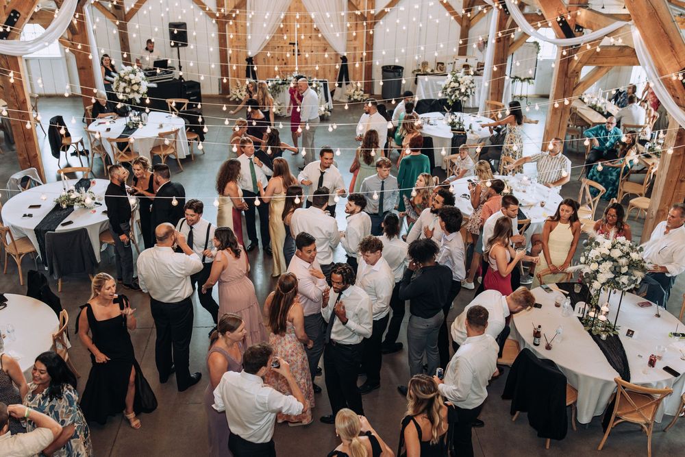 Aerial view of wedding guests mingling and dancing in a beautifully decorated rustic barn reception venue.