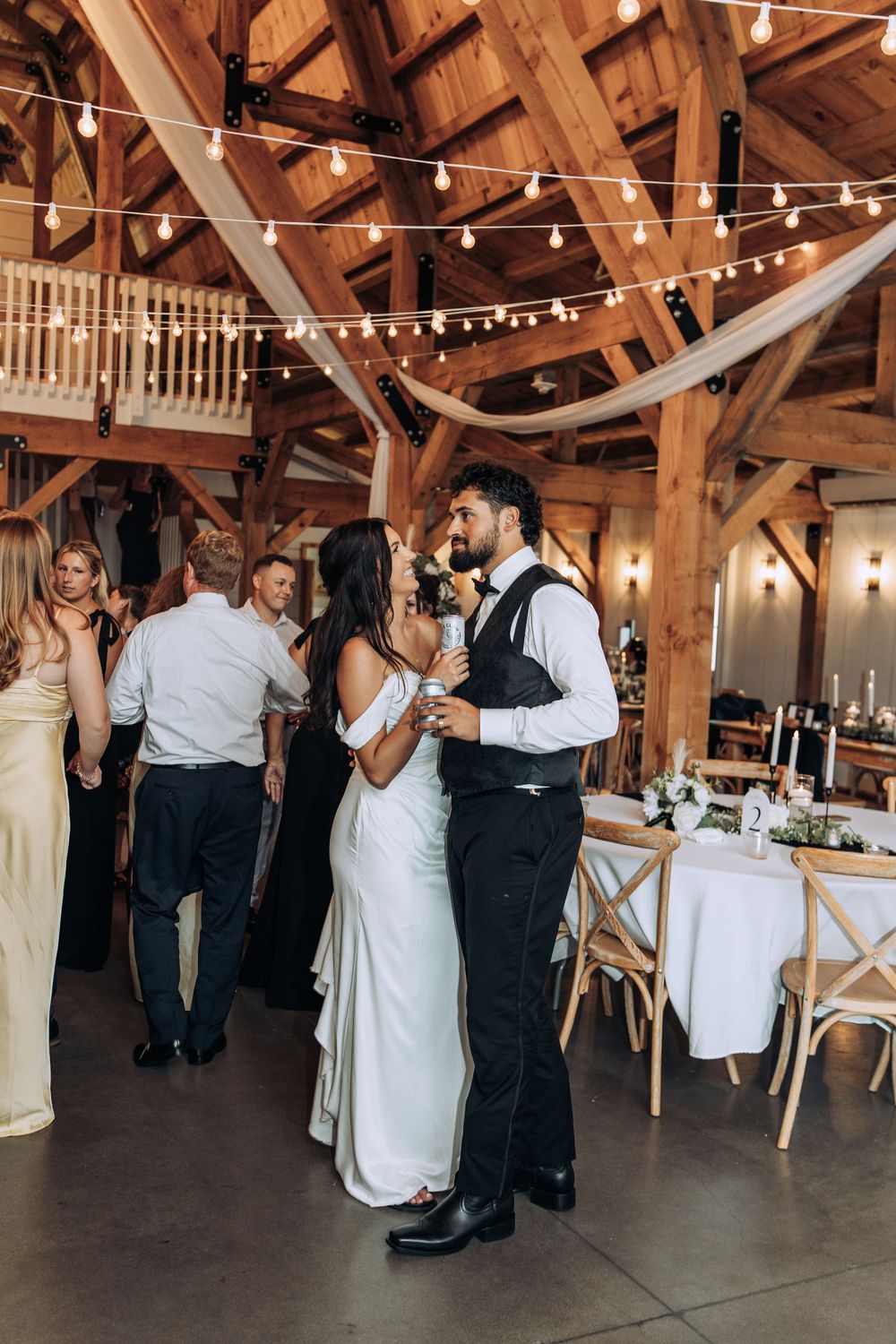 Bride and groom sharing first dance at rustic barn wedding reception with warm string lights overhead.