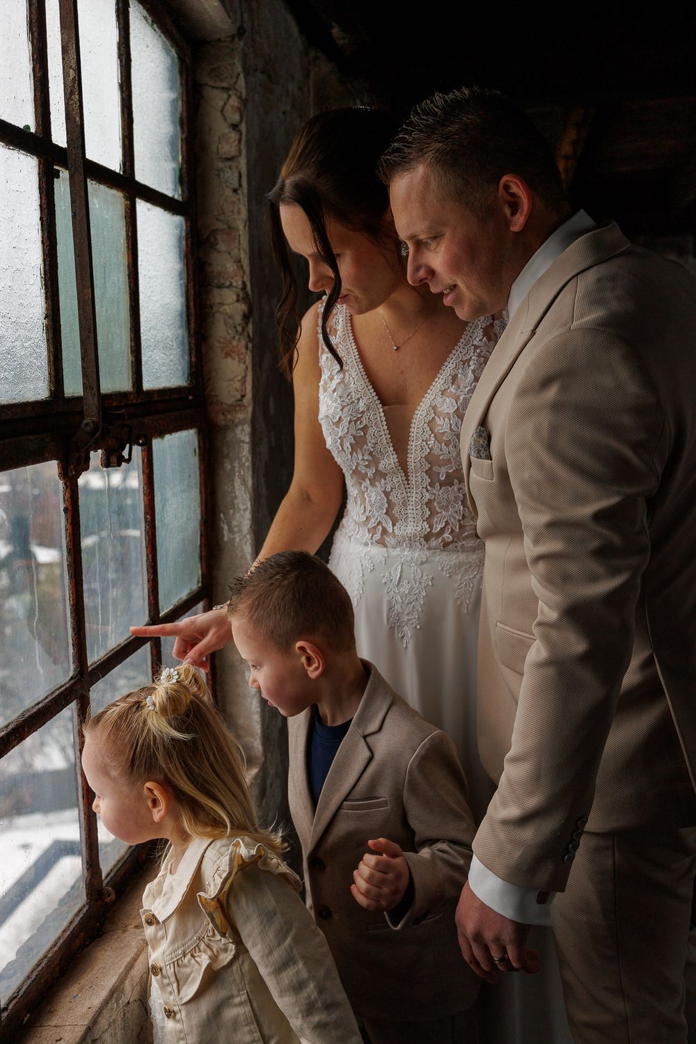 Bruidspaar en kinderen kijken uit het raam lachend - industriele stoere trouwfotoshoot  - Pand127 - Rijen - MaxFotos