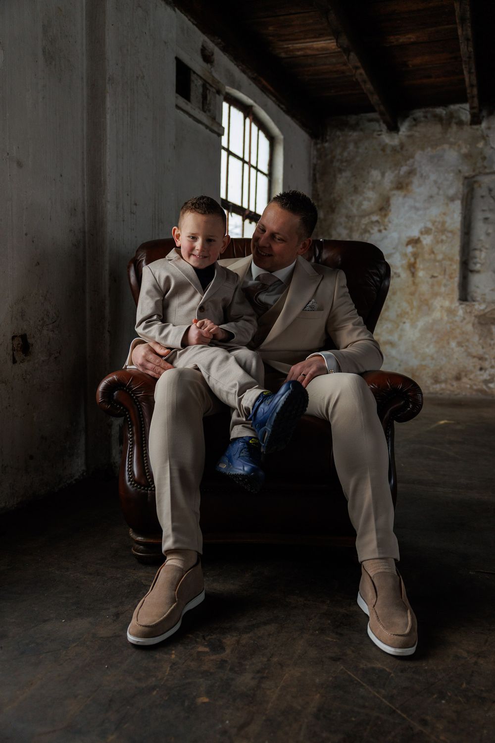 Bruidegom met zoontje op leren herenstoel tijdens industriele en stoere trouwfotoshoot - Pand127 - Rijen - MaxFotos