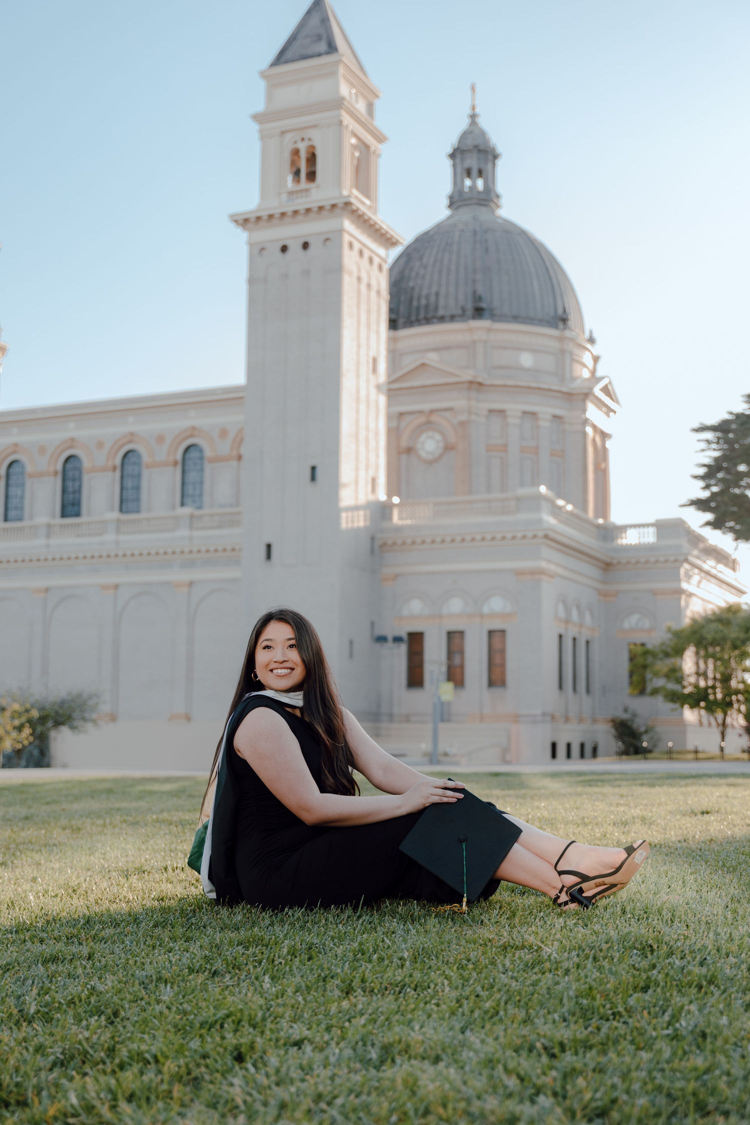 Graduate in masters hood sits on grass in front of St. Ignatius Church at the University of San Francisco.