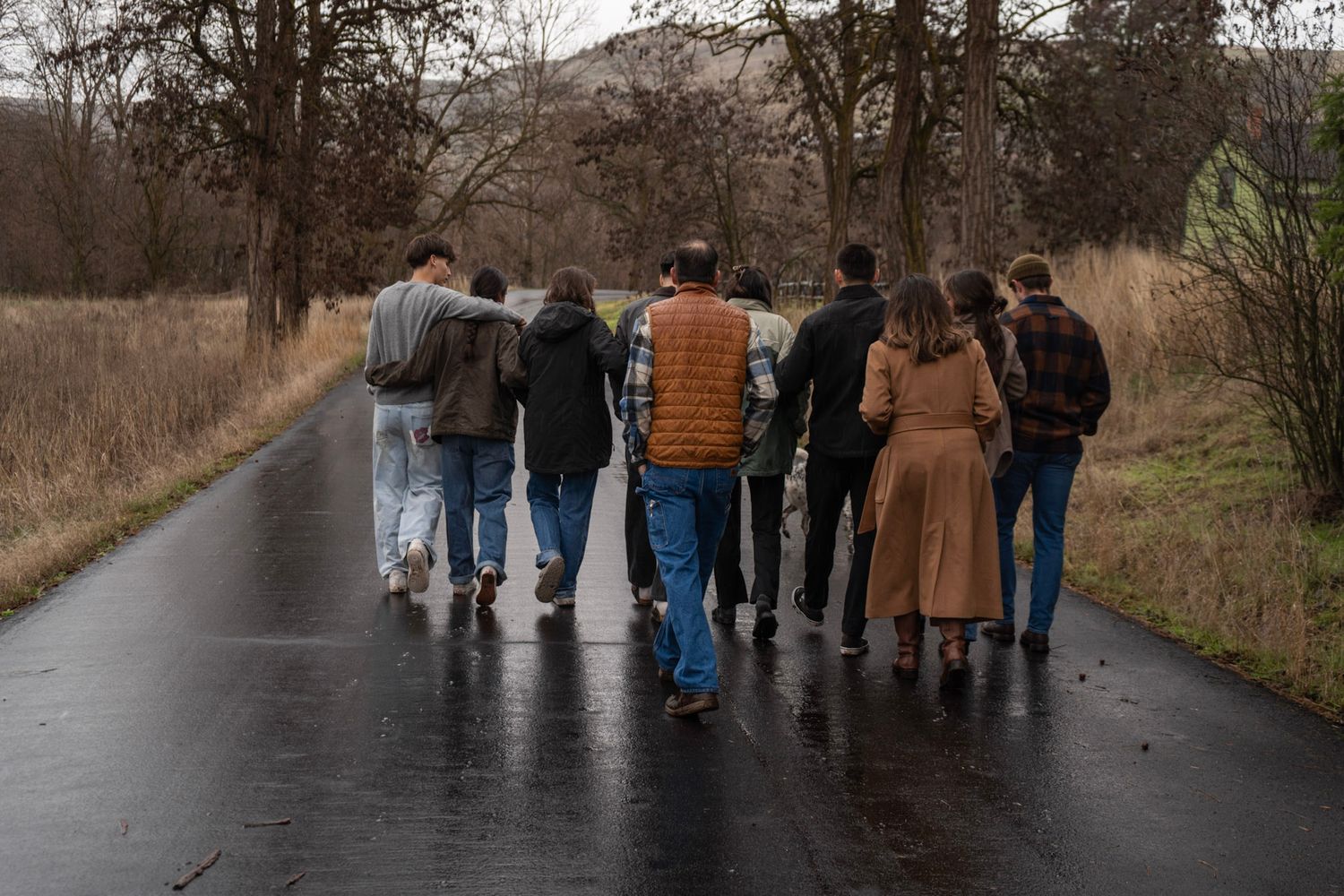 People walking together on a wet paved path through an autumn landscape.