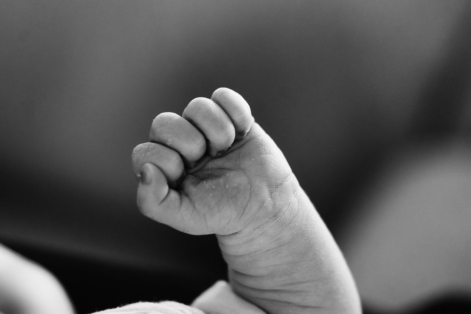 A black and white close-up photo shows tiny baby feet against a dark background.