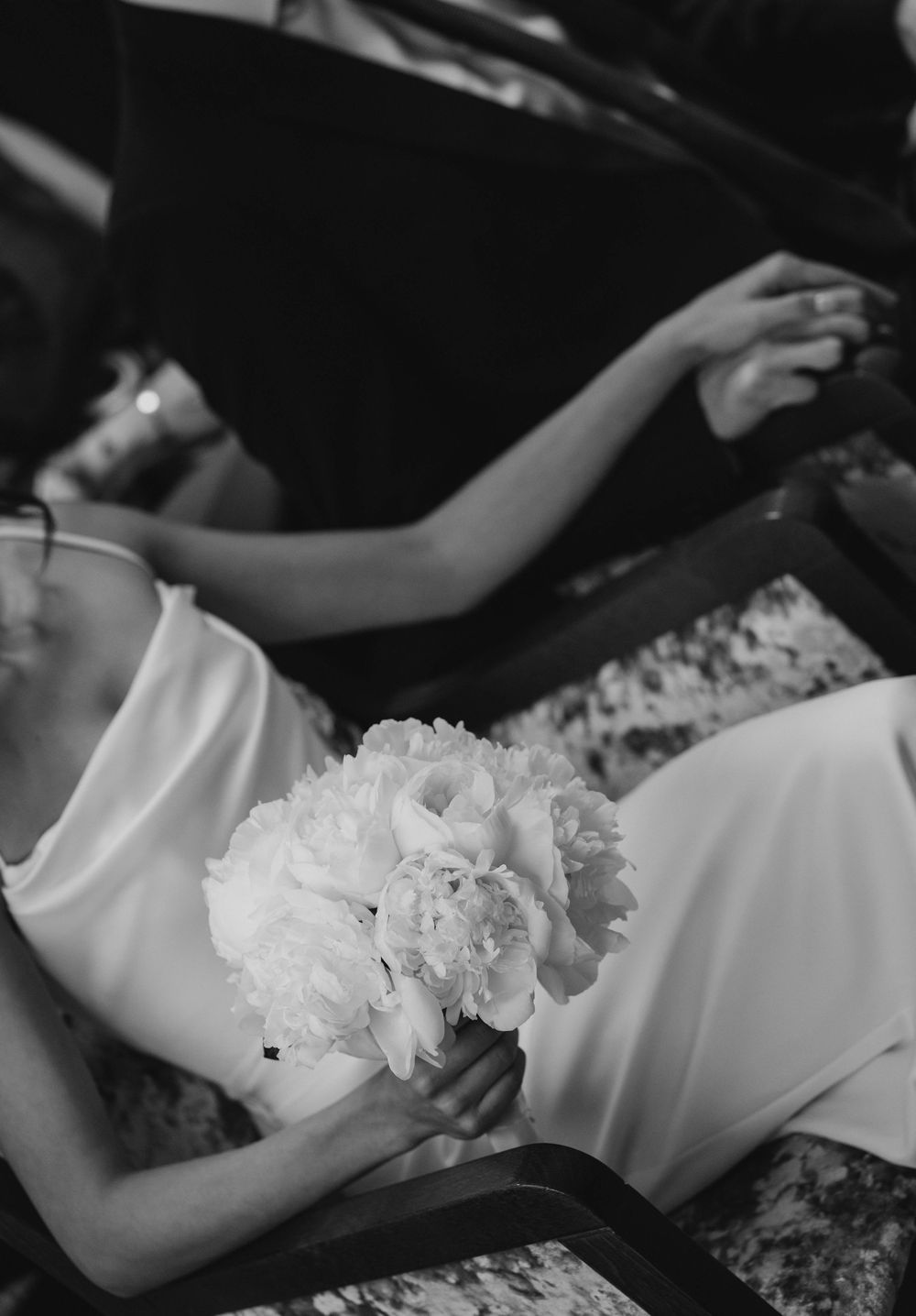 An elegant black and white photo featuring a white peony bouquet and satin dress.