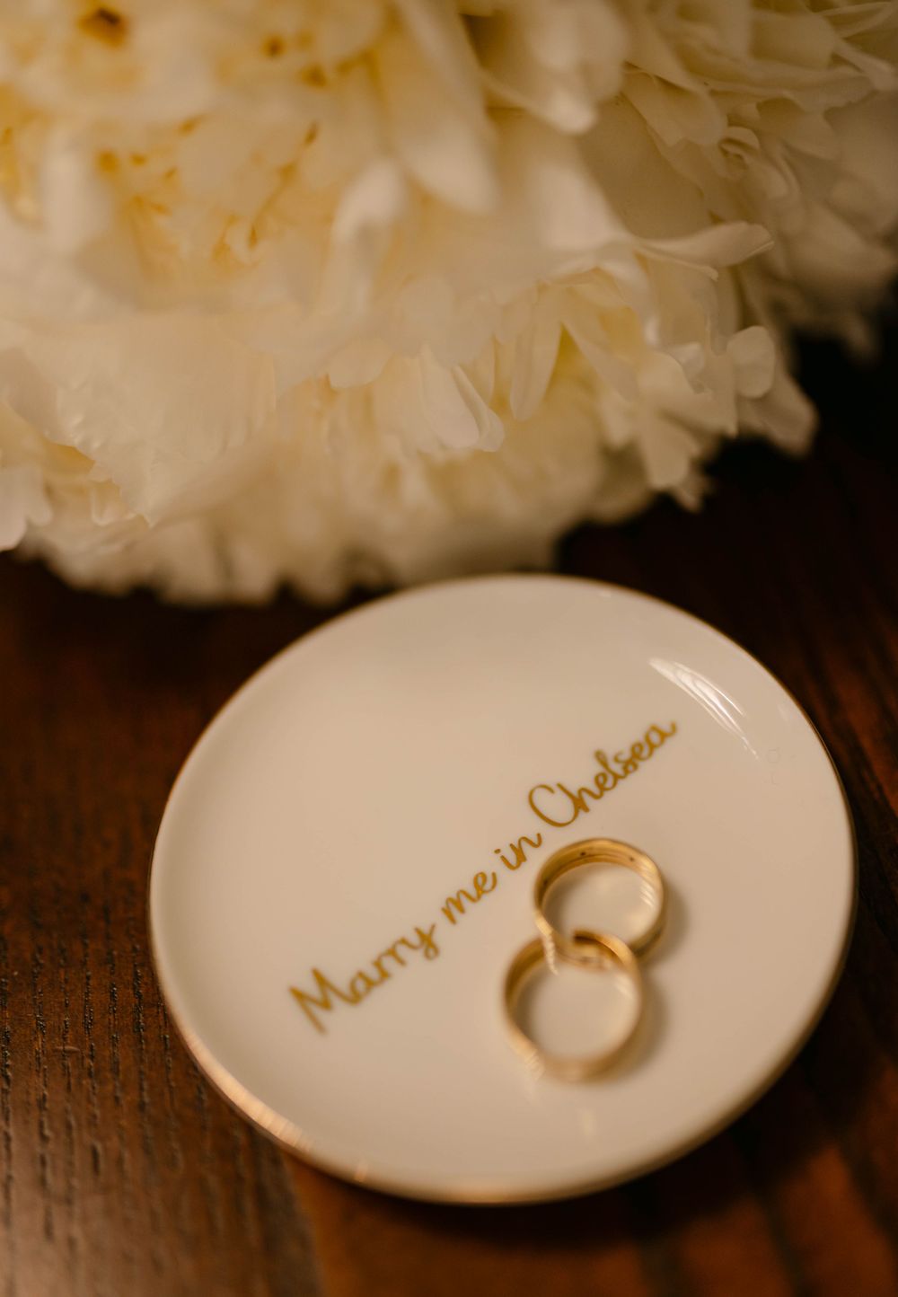 Two gold wedding rings on a white dish with 'Marry me Chelsea' inscription.