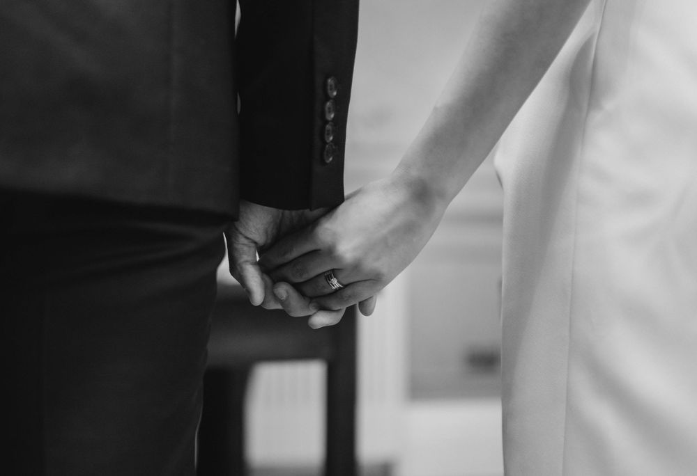 A black and white close-up of newlyweds holding hands.