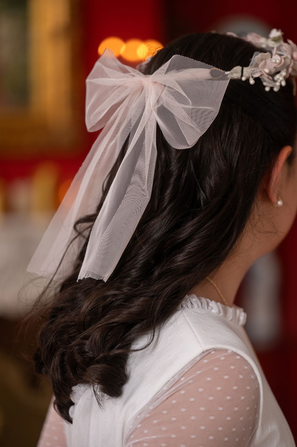 Close-up view of a delicate white tulle bow and floral hair accessory adorning dark wavy hair at a wedding.