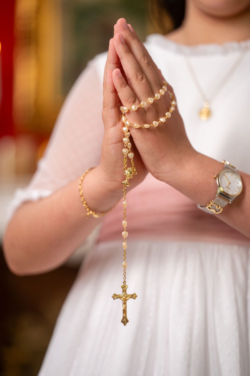 Close-up sequence showing hands holding and praying with a gold rosary against a white dress background.