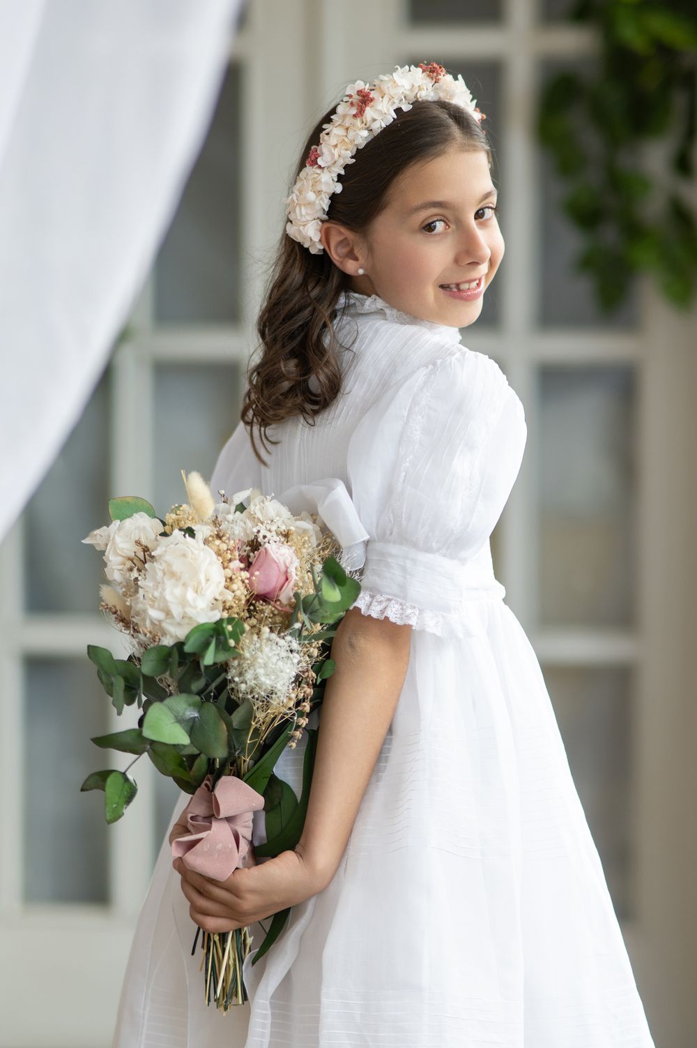 Young girl in white first communion dress holding pink and white floral bouquet smiles in series of photos.