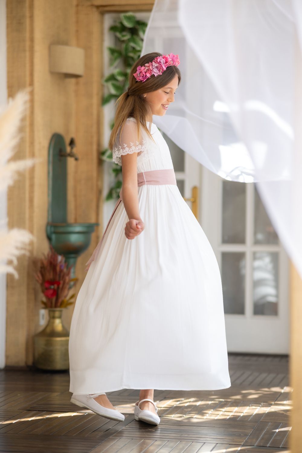 A flowing white dress and delicate shoes move gracefully across a sunlit wooden floor.