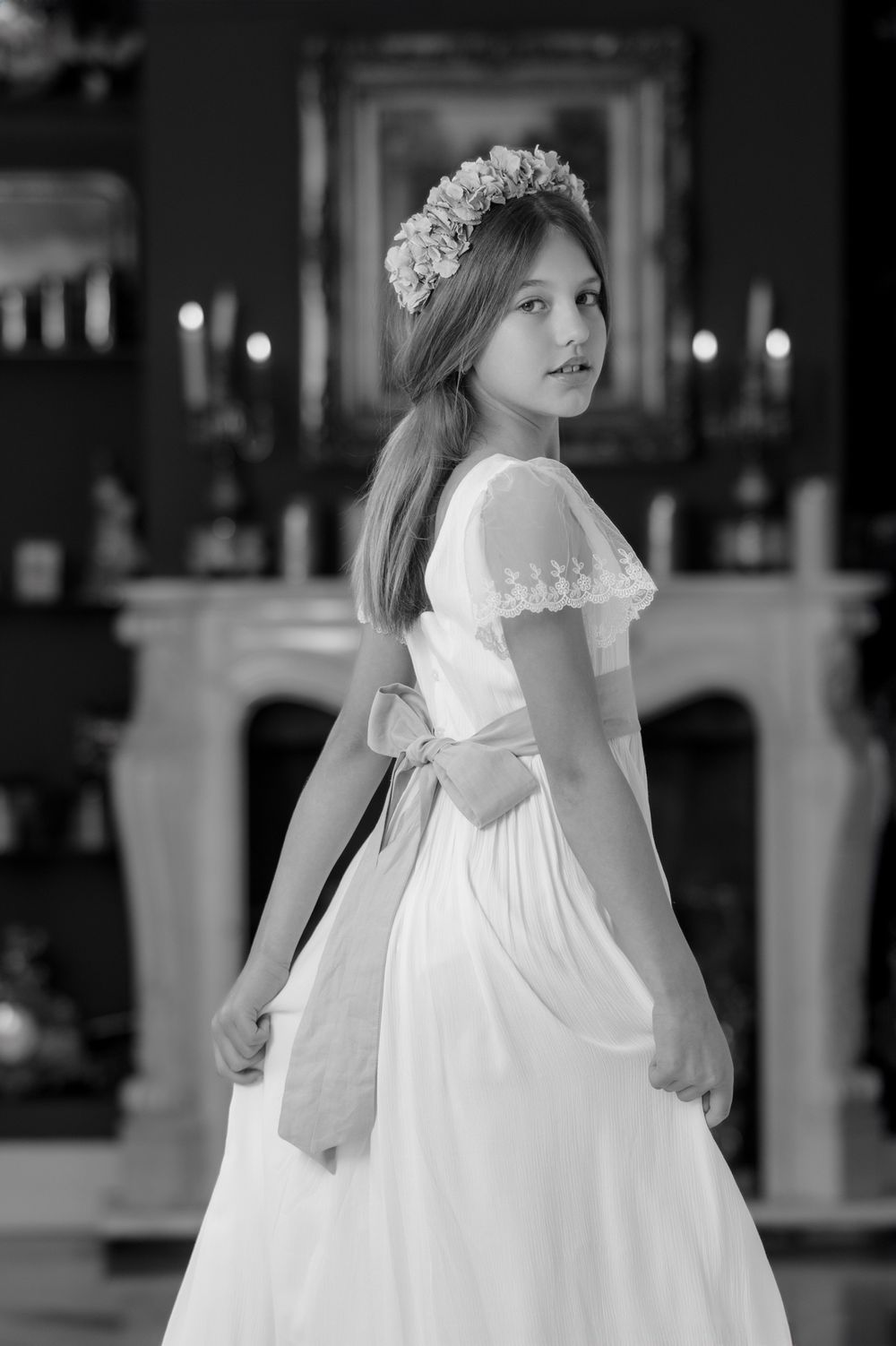 A series of black and white photos showing a young child in a white communion or flower girl dress with floral crown details.