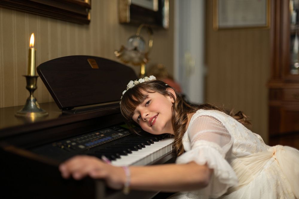 A pianist in a white dress lies gracefully across the piano keys in an artistic performance pose.