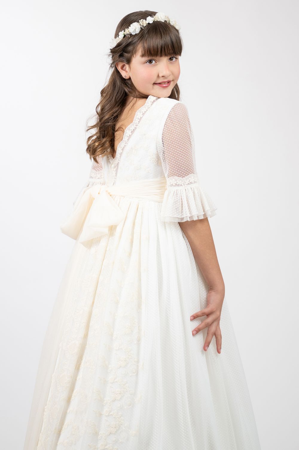 A young girl wears a flowing white dress with sheer sleeves and ruffled details shown from multiple angles.