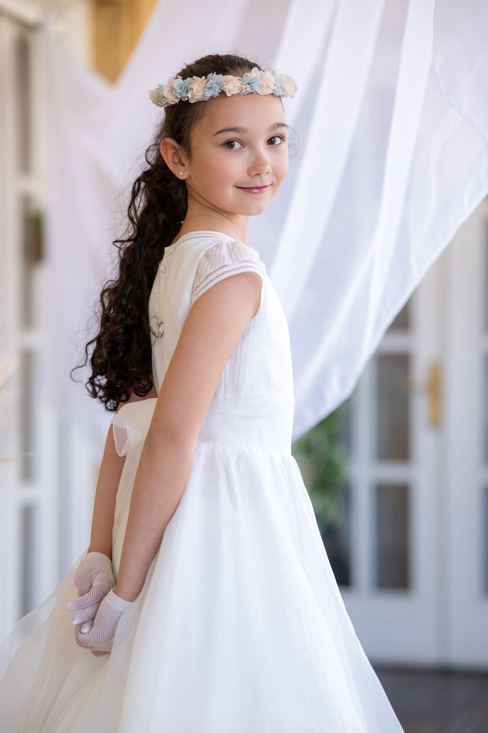 A young flower girl in a white dress and floral headpiece poses gracefully in a series of photos.