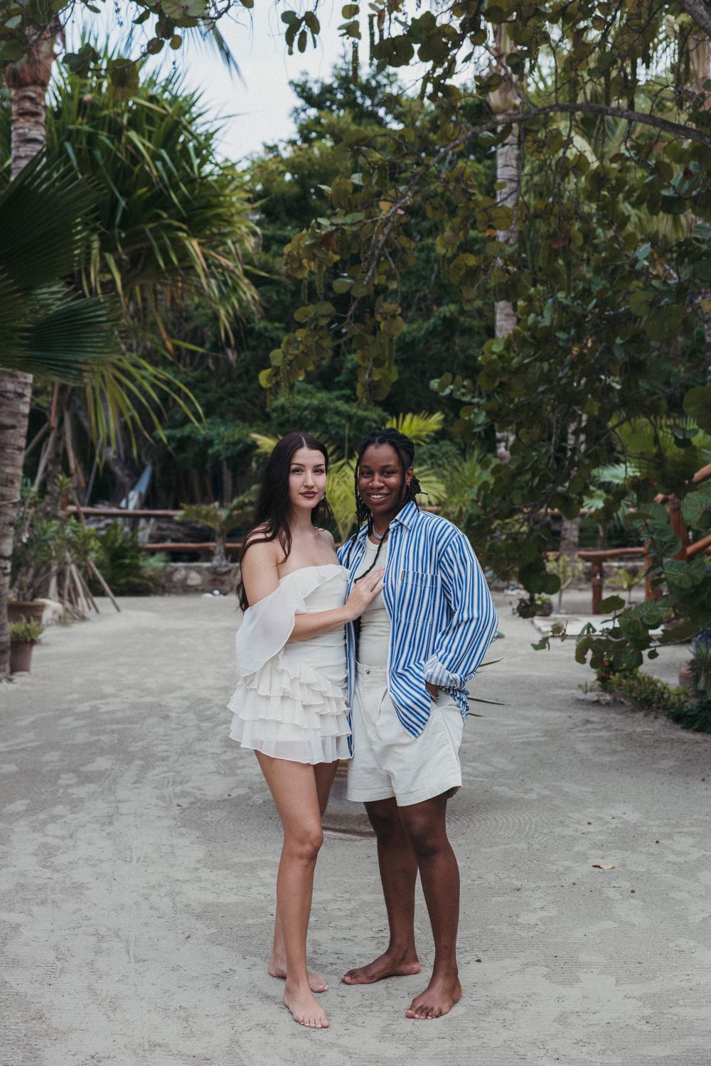 A couple poses together on a sandy beach path lined with tropical palm trees and lush vegetation at Tierra del Mar Hotel in Holbox Mexico