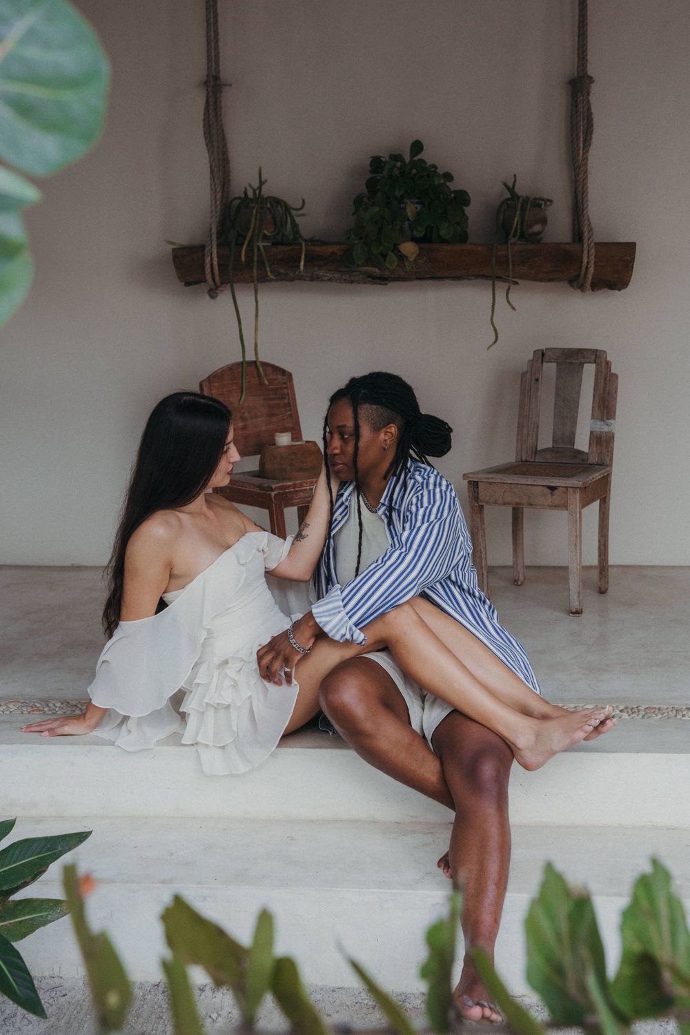 Two people sitting intimately on a porch with plants and rustic decor in a bohemian setting, belonging to the hotel Tierra del Mar Holbox Mx
