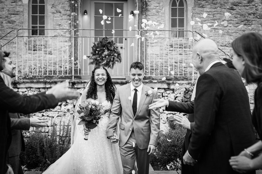 Wedding party celebrating in front of a rustic stone building with gothic windows.