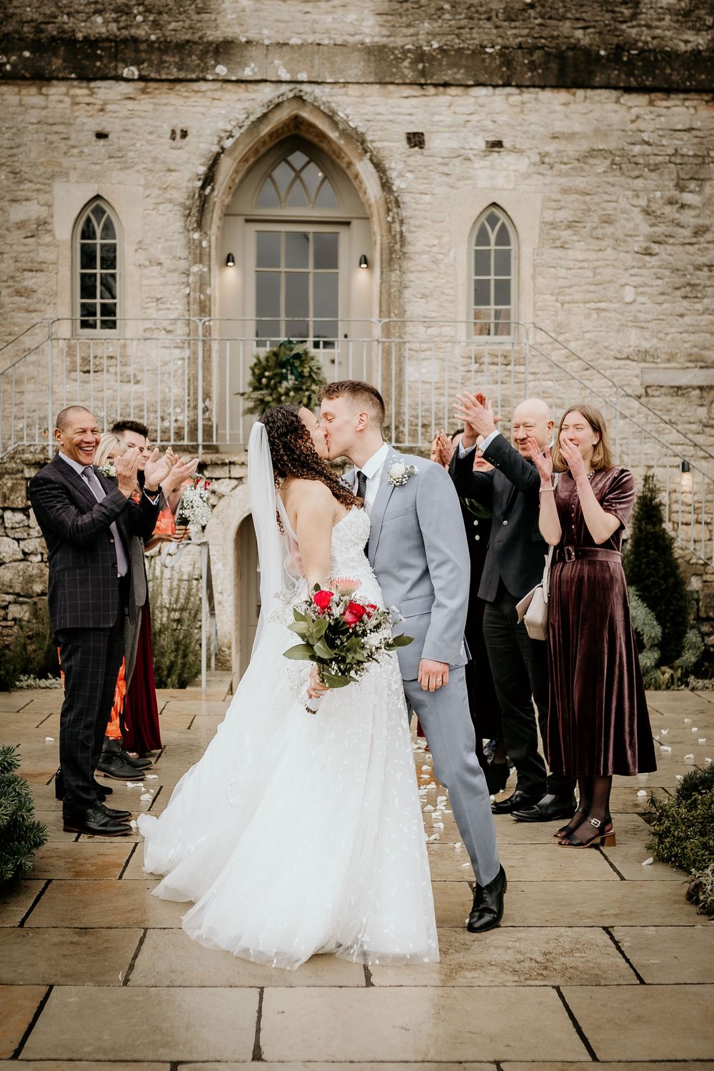 Wedding couple dances surrounded by guests outside a historic stone church building.