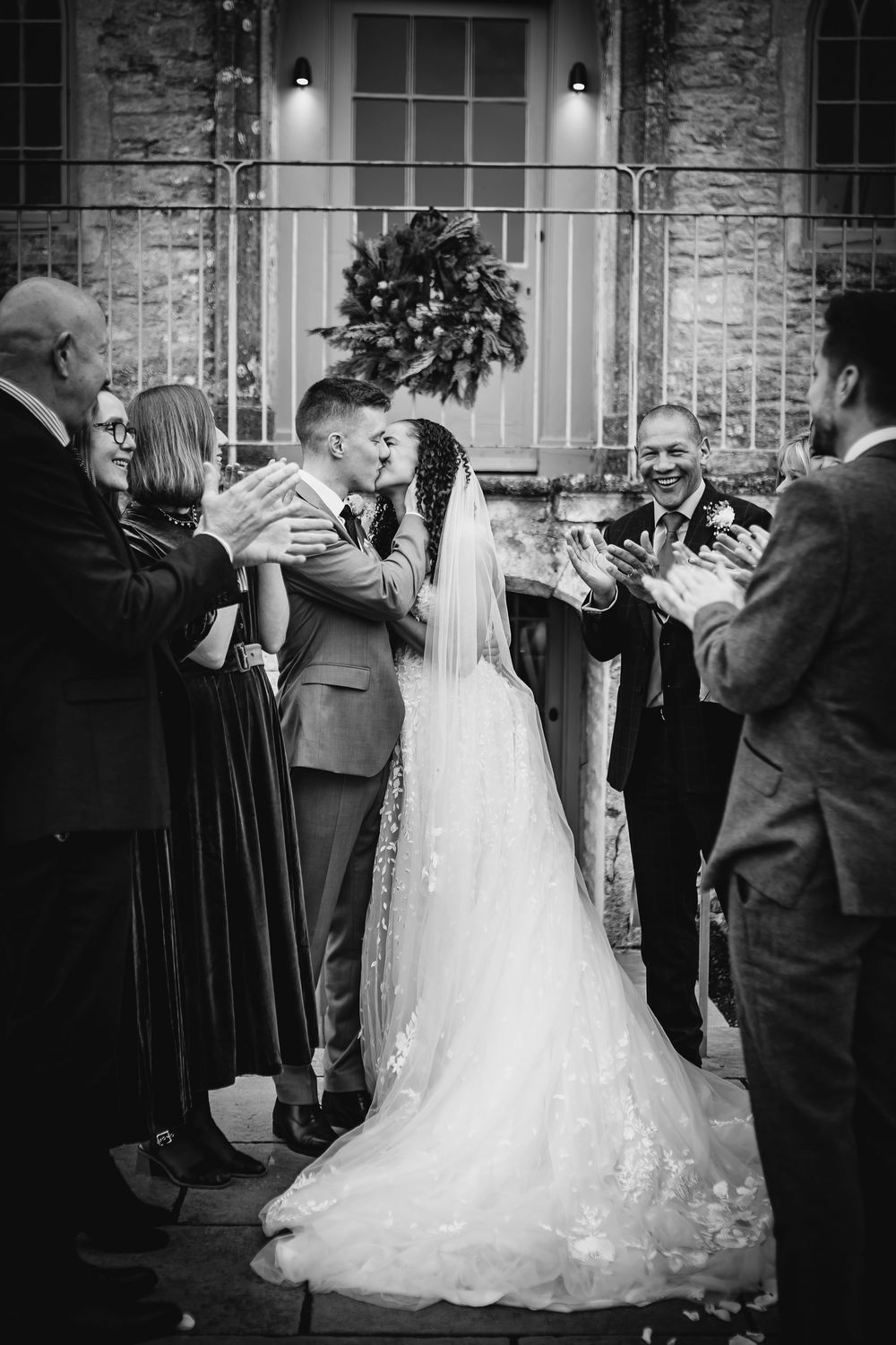 A sequence of black and white photos showing a wedding couple dancing with guests at a stone building venue.