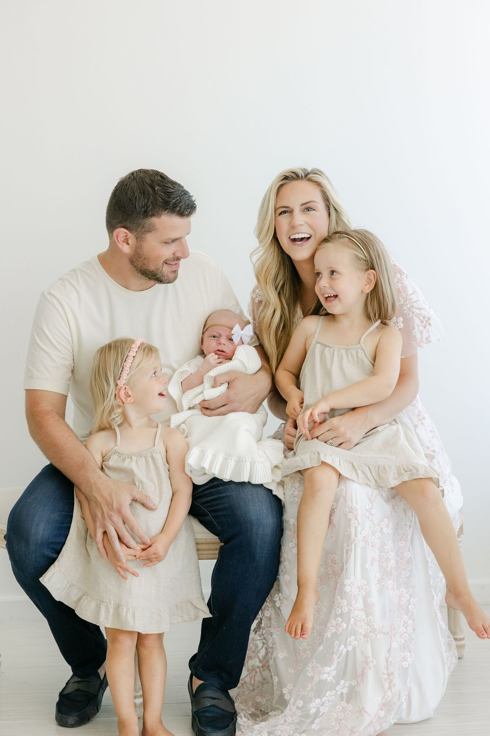 Family portrait session in white and cream tones showing playful interactions with a baby.