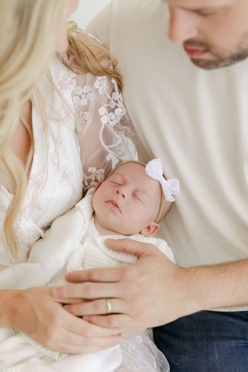 Tender family moments with a sleeping newborn wearing white against a neutral background.