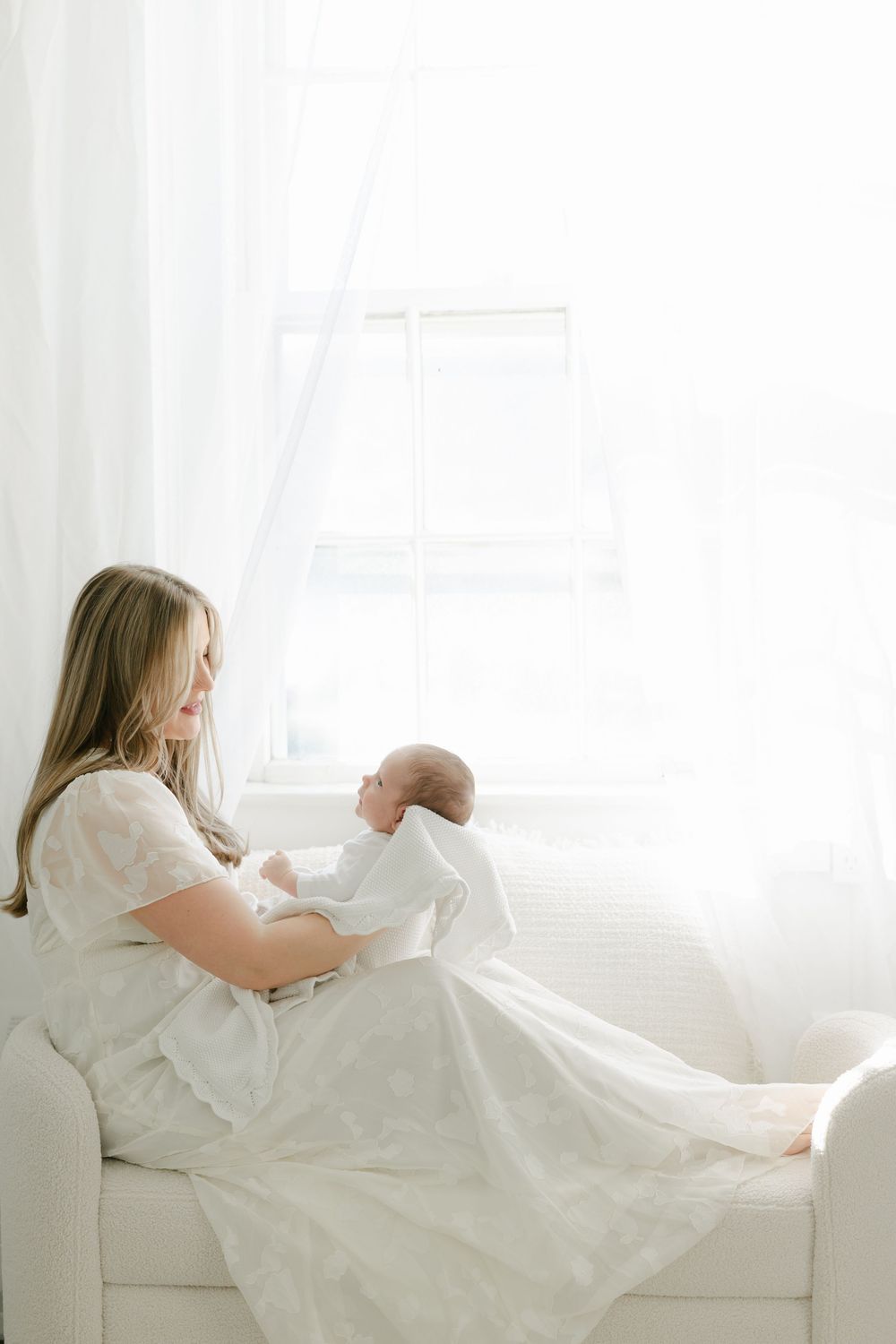 A tender moment captured in white tones as someone holds a newborn on a couch.