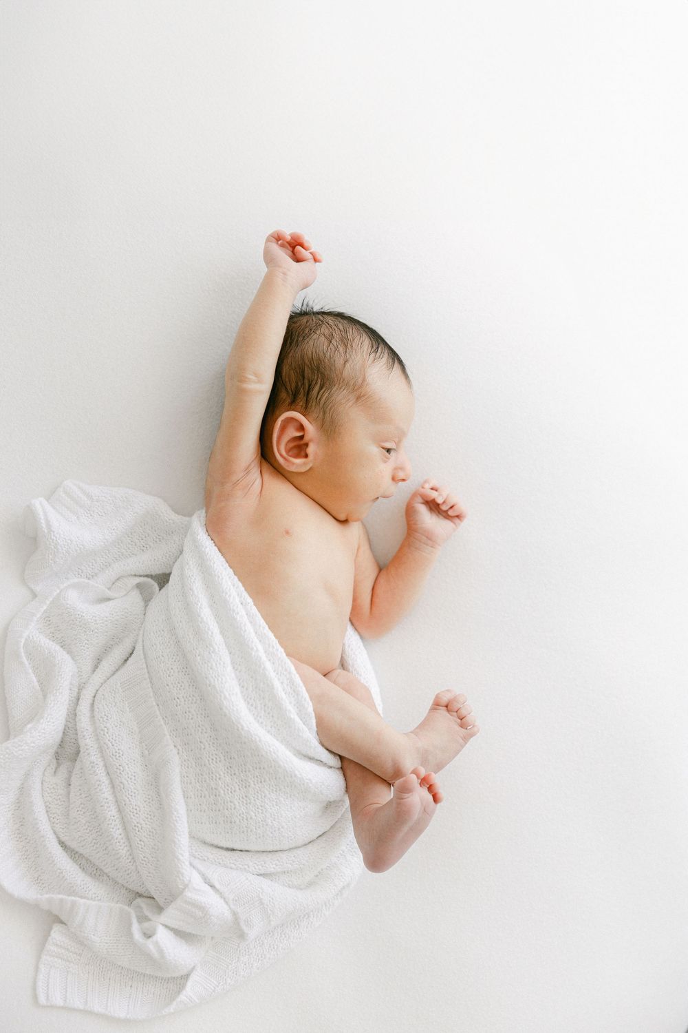 Newborn baby wrapped in white blanket sleeping peacefully on white background.