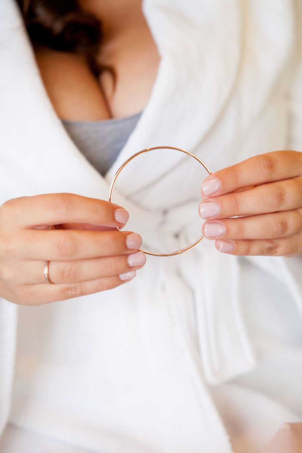 Hands gently holding a thin copper or rose gold wedding band against a white background.