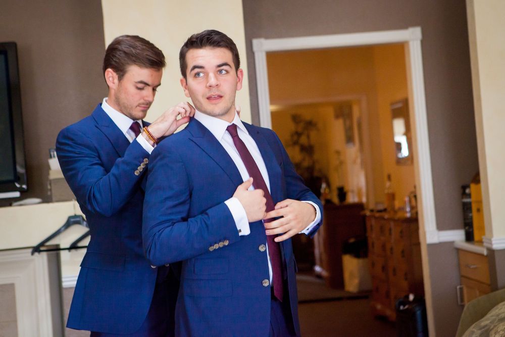 Groomsmen in navy blue suits and burgundy ties sharing a candid moment.