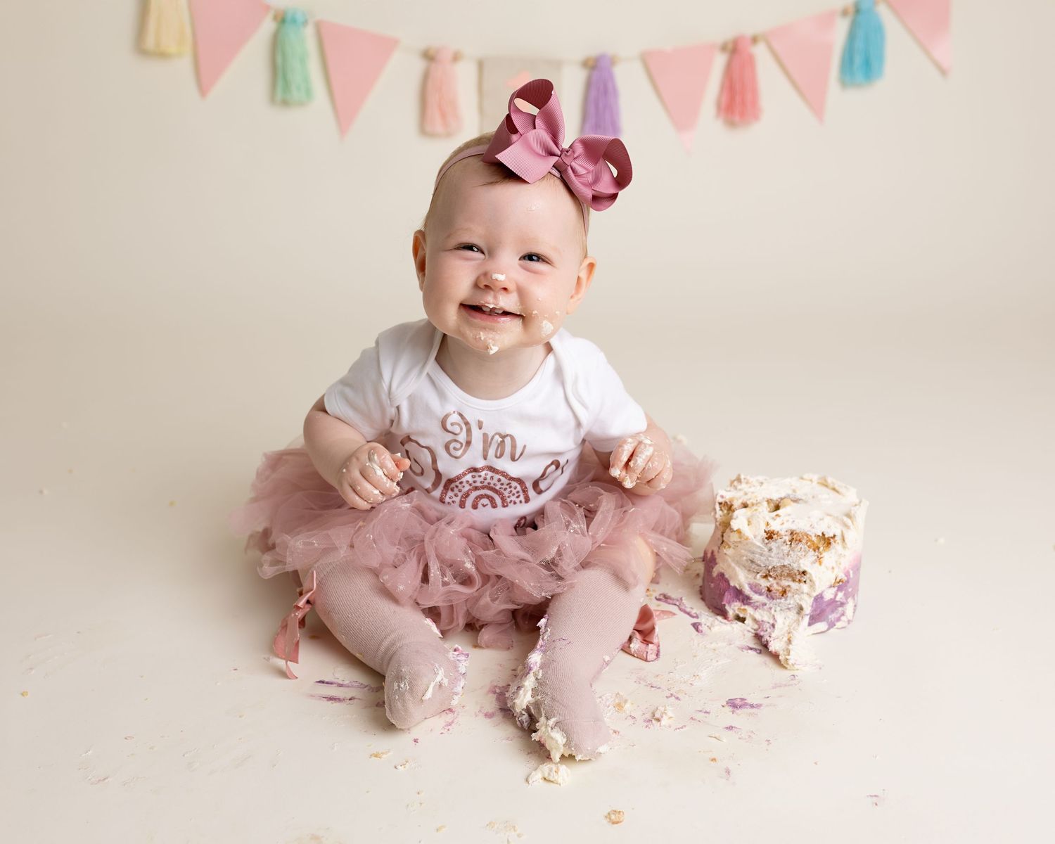 One year old baby girl smiles cutely aat the camera during her messy fun cake smash session with pink cake, Renfrewshire