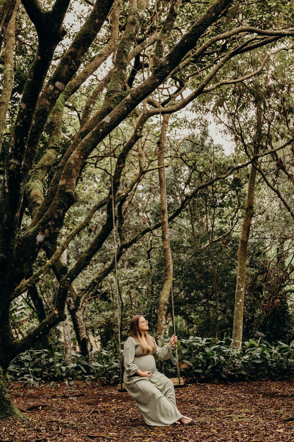 A couple shares an intimate moment while sitting on a swing in a wooded forest setting.