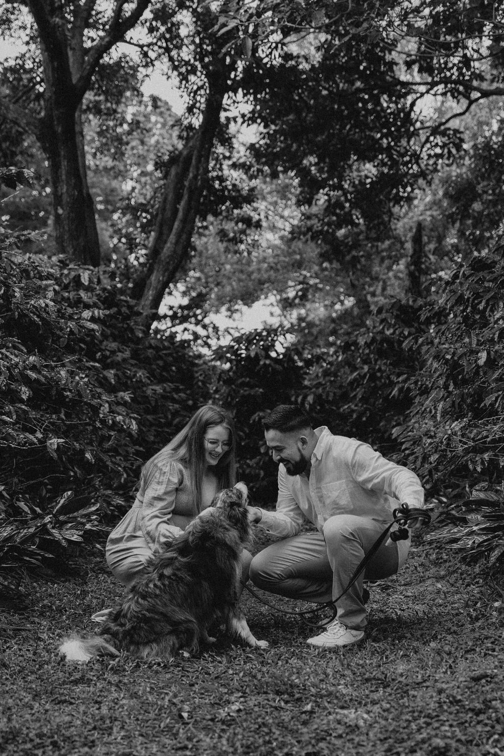 A playful scene unfolds in a forest setting as a couple lies on the ground with their dog.