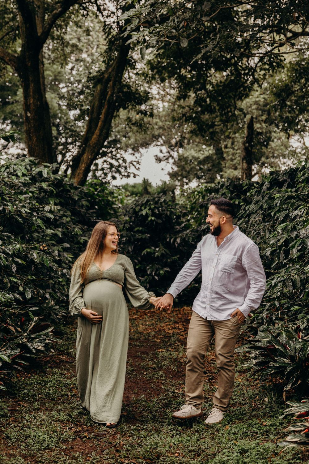 A couple shares a playful moment in a lush green forest setting during an outdoor photoshoot.