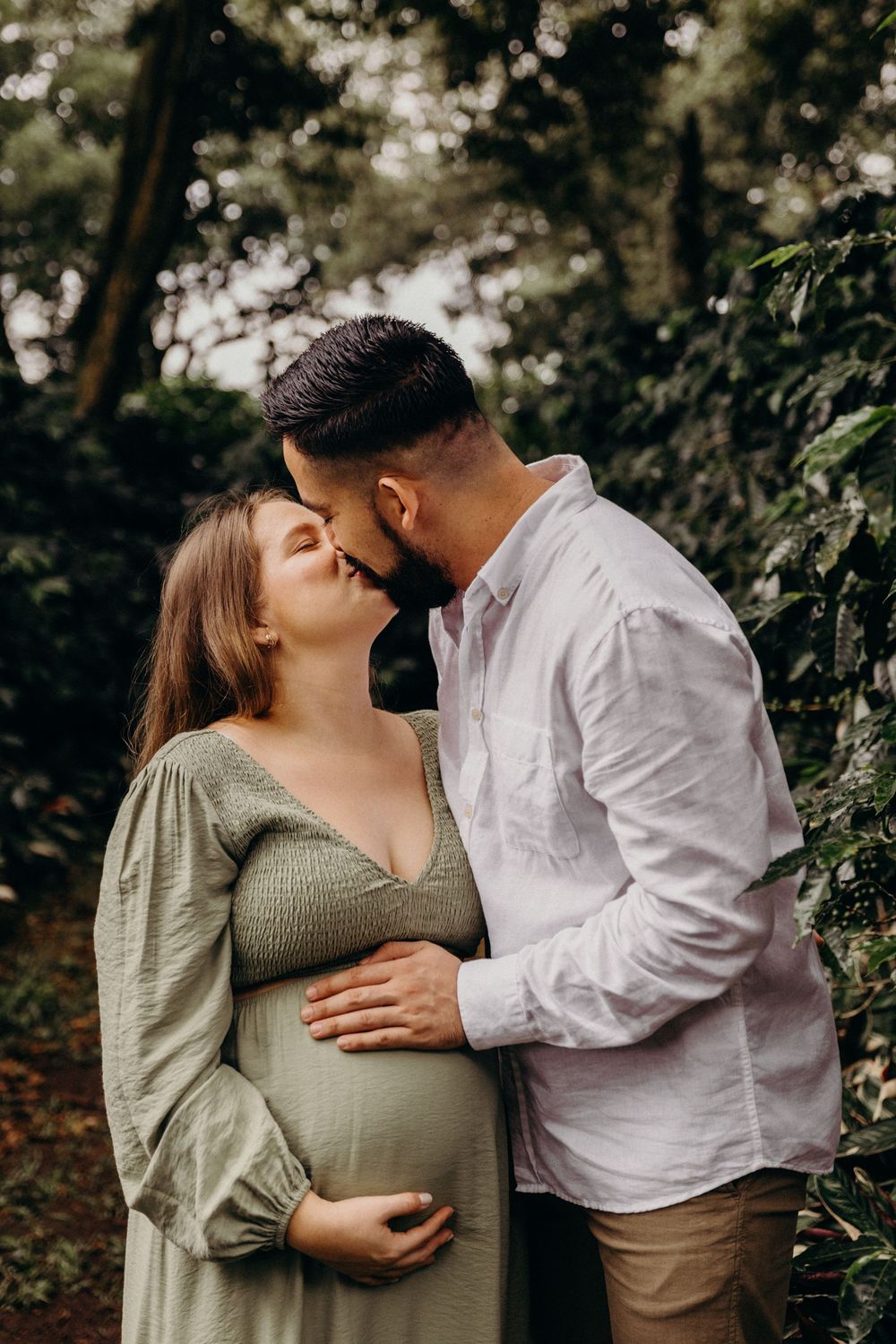 An expectant couple embraces tenderly in a wooded setting during their maternity photo session.