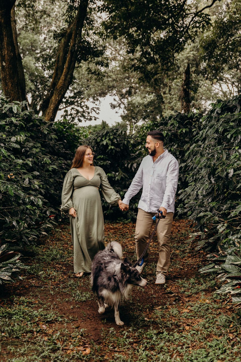 A couple walks through a wooded trail with their fluffy dog on an autumn day.