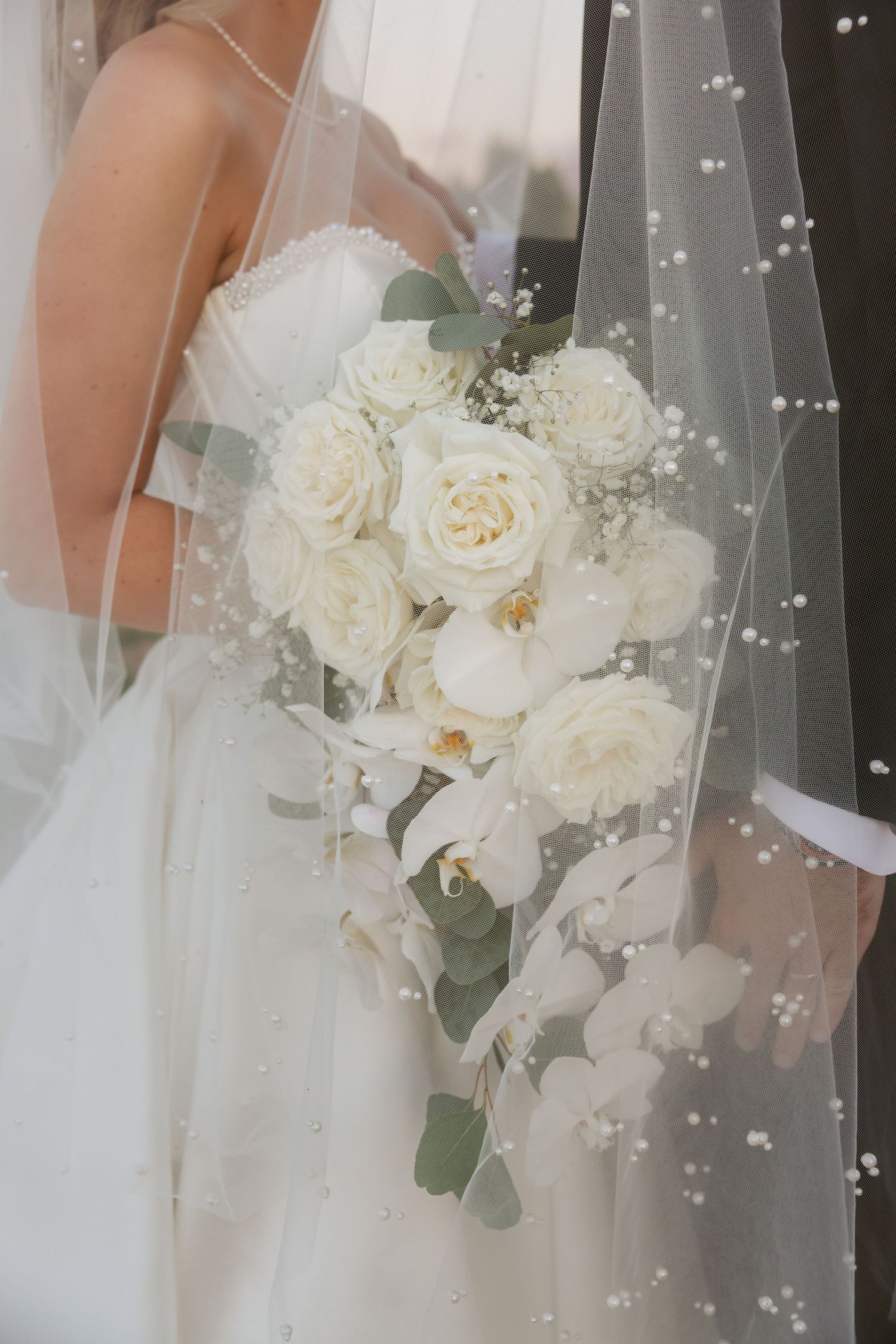 Close-up of an elegant white bridal bouquet with roses and delicate veil details.