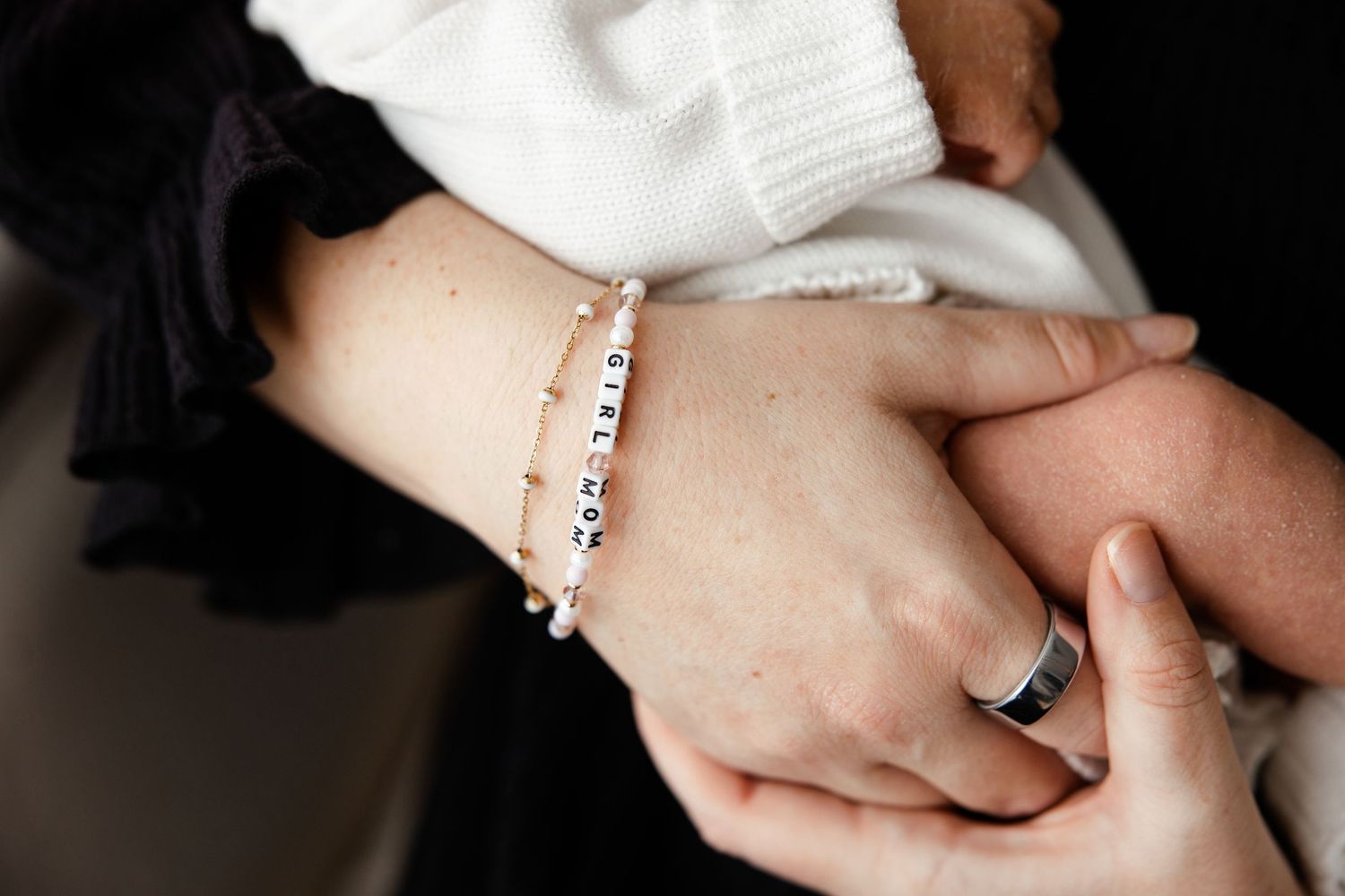 Close-up of hands wearing delicate beaded bracelet saying girl mom holding newborn baby