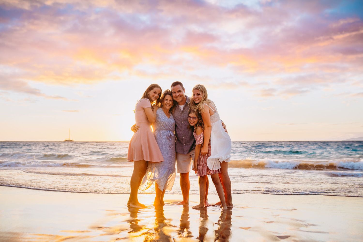 Kihei family photographer. Family beach portrait session with golden sunset sky and crashing waves in background.
