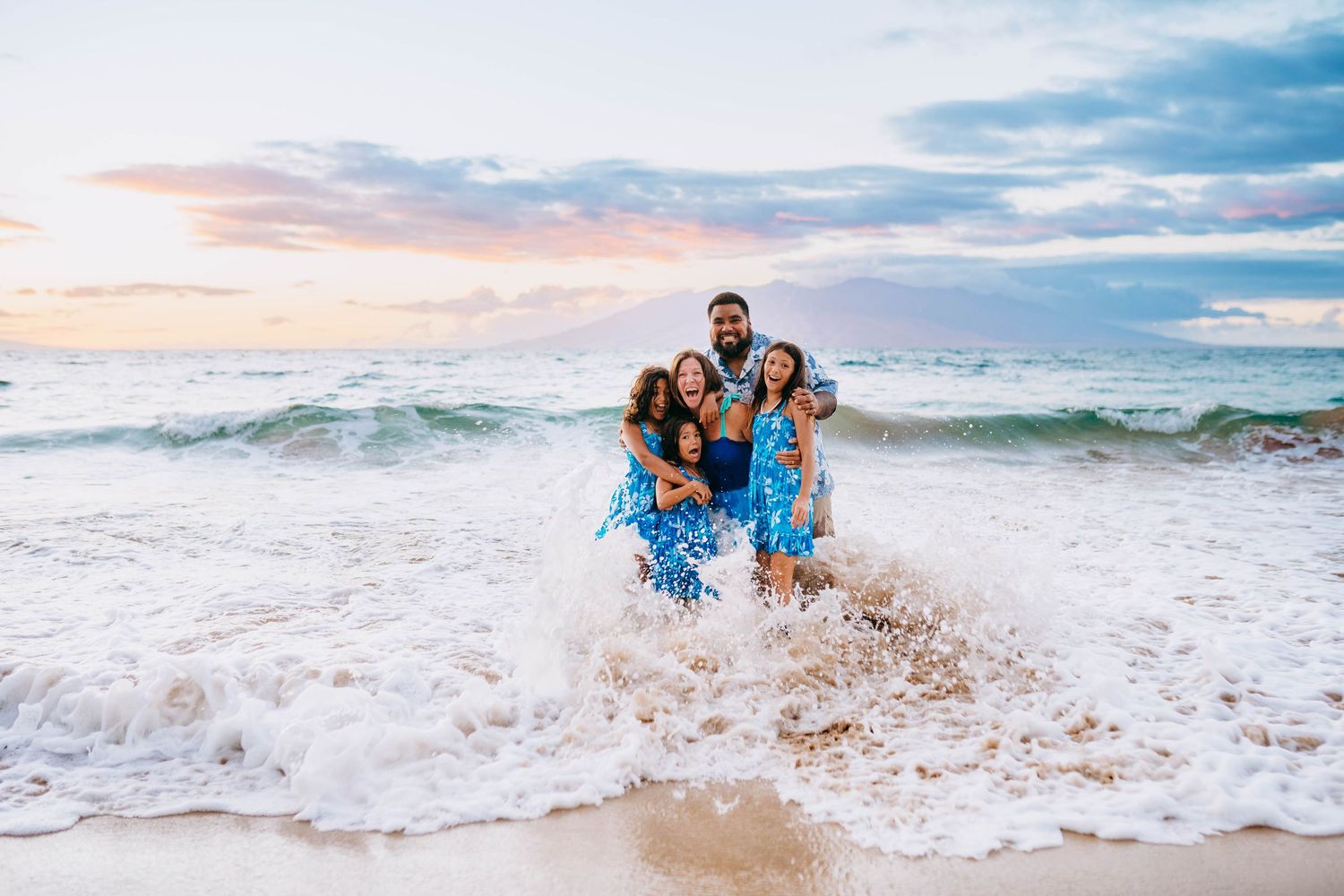 Makena family photography. Family playing and splashing in ocean waves during beach photoshoot at sunset.