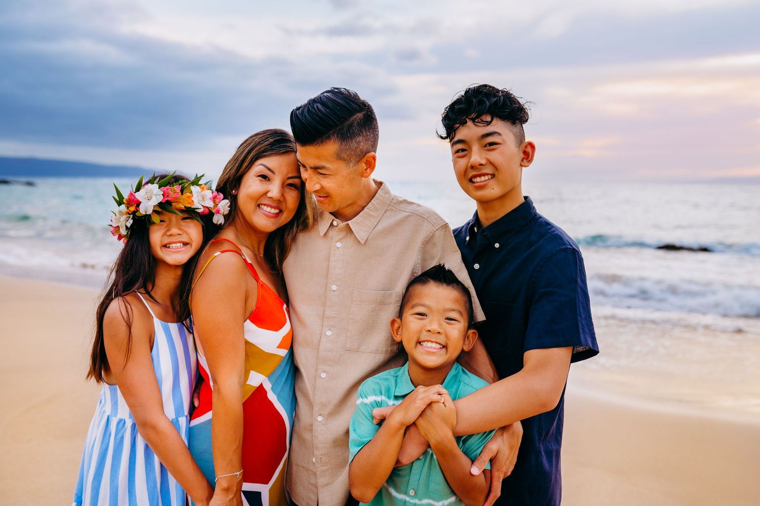 Maui family photographer capturing a sunset beach family session. Joyful family beach photos with colorful outfits against dramatic sunset