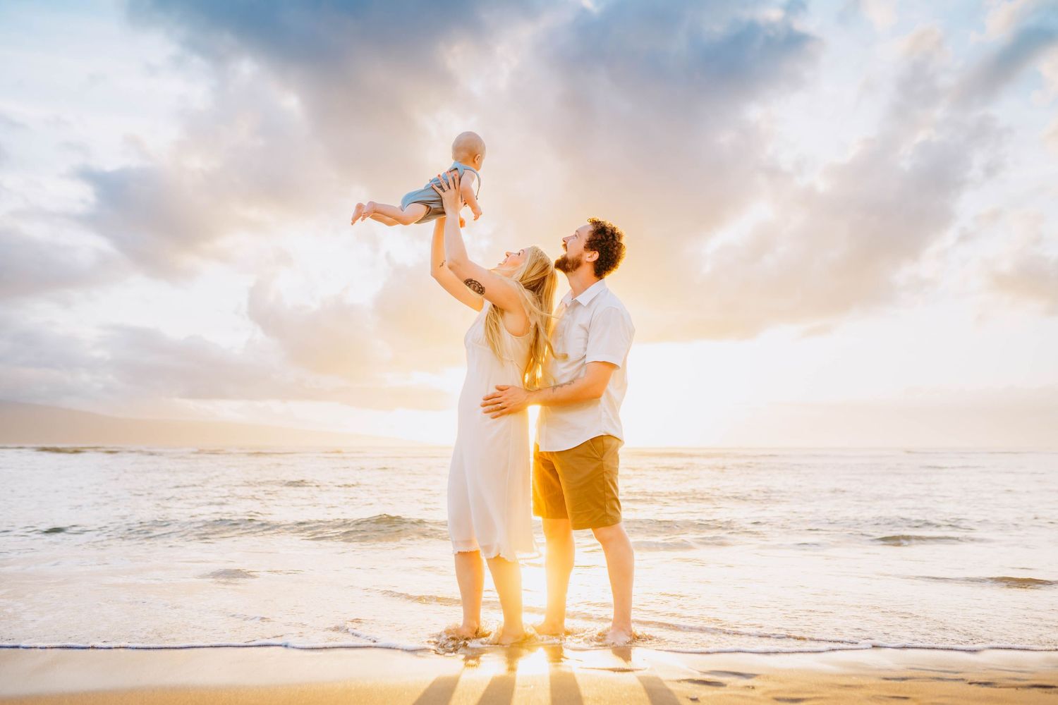 Maui family photographer capturing a sunset beach family session. Family silhouettes walking along beach shoreline at golden hour.