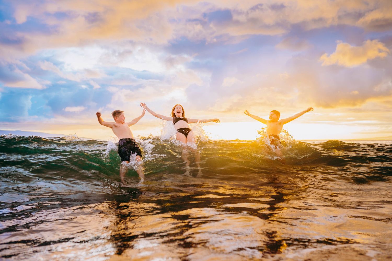 People splashing and playing in ocean waves during vibrant sunset family photography in maui playing in the water