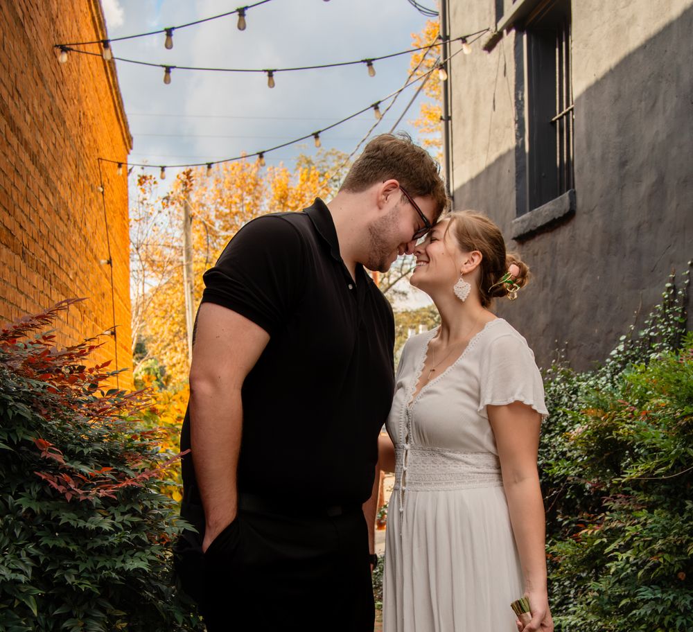 Romantic couple in formal attire share intimate moments against a brick wall with string lights overhead.