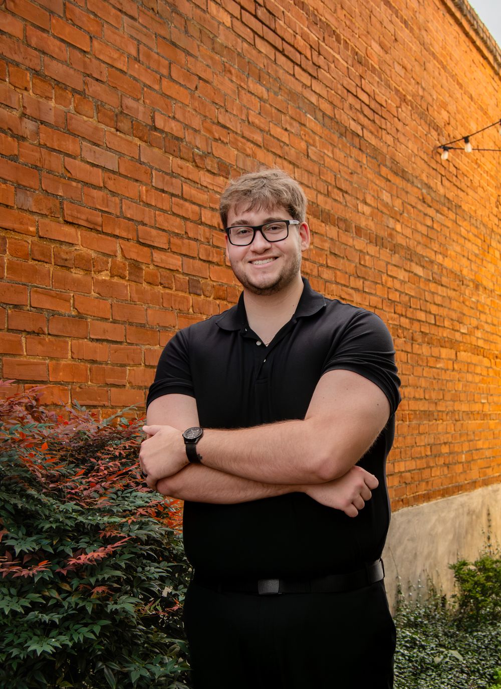 Portrait series against a warm-lit brick wall featuring someone in black attire.