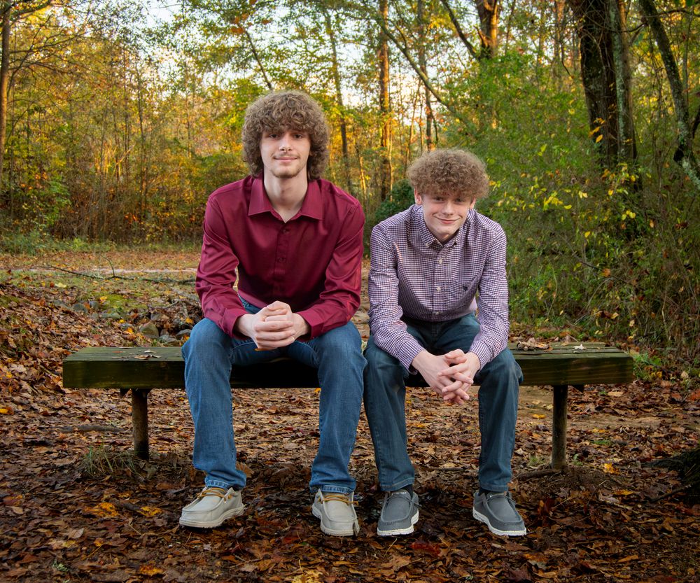 two brothers sitting casually on a seat surrounded by autumn leaves.