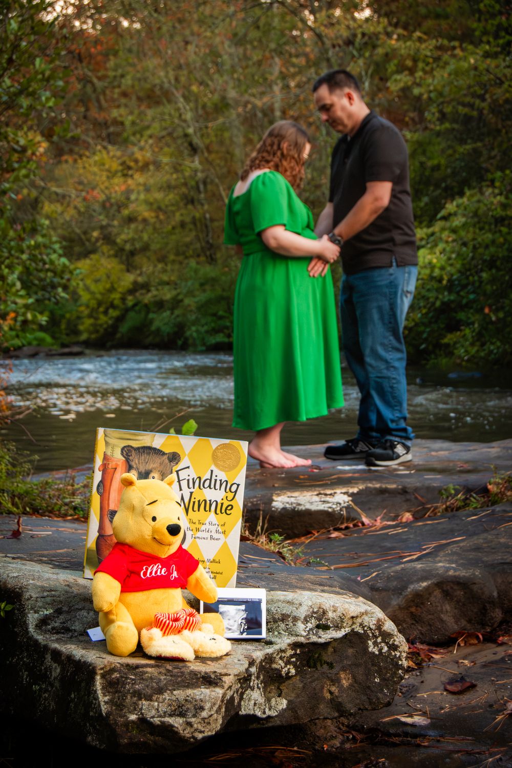 Maternity photoshoot setup with Winnie the Pooh themed props by a river.