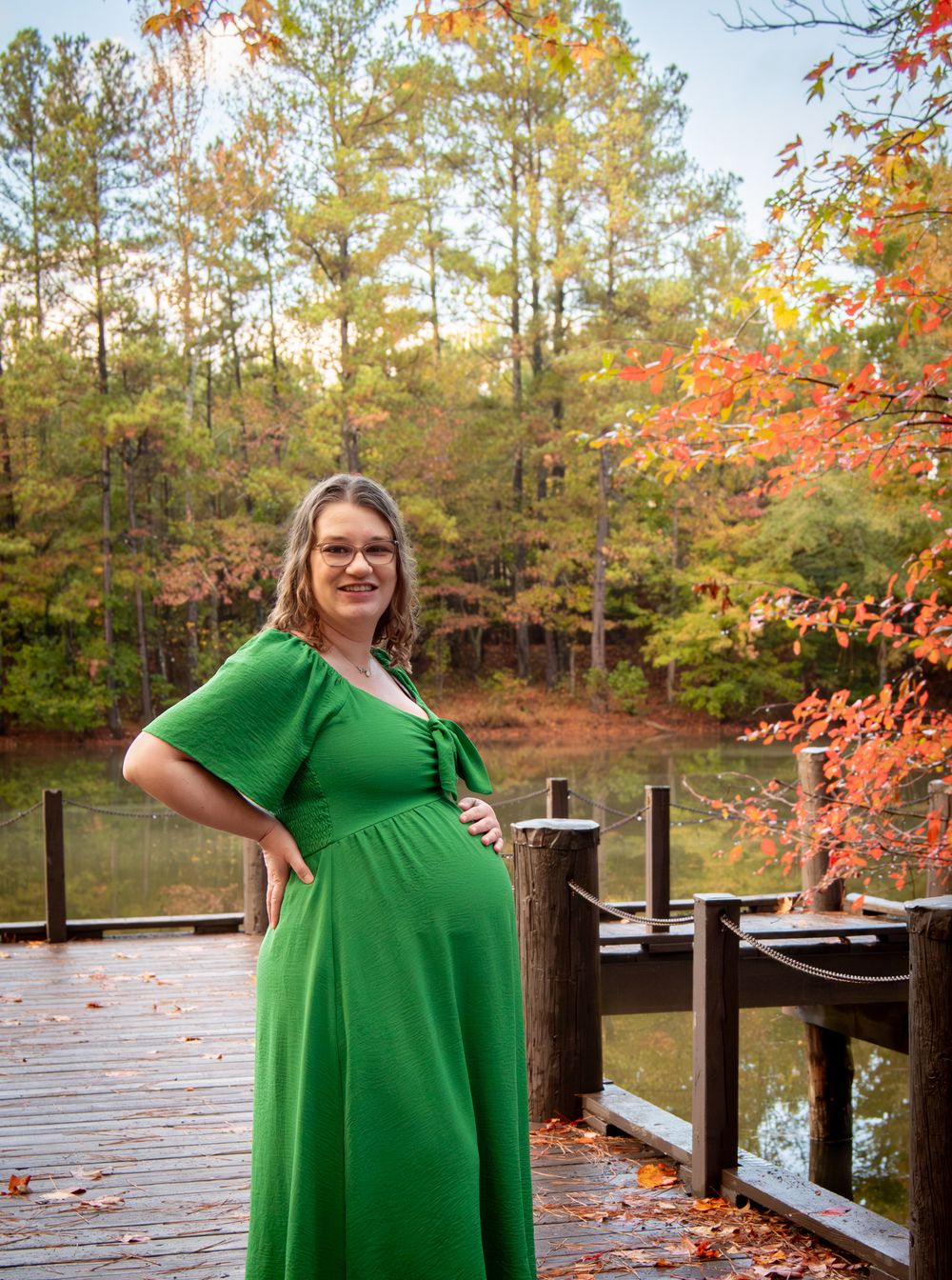 Maternity photos on a wooden deck showing a person in an emerald green dress during fall.